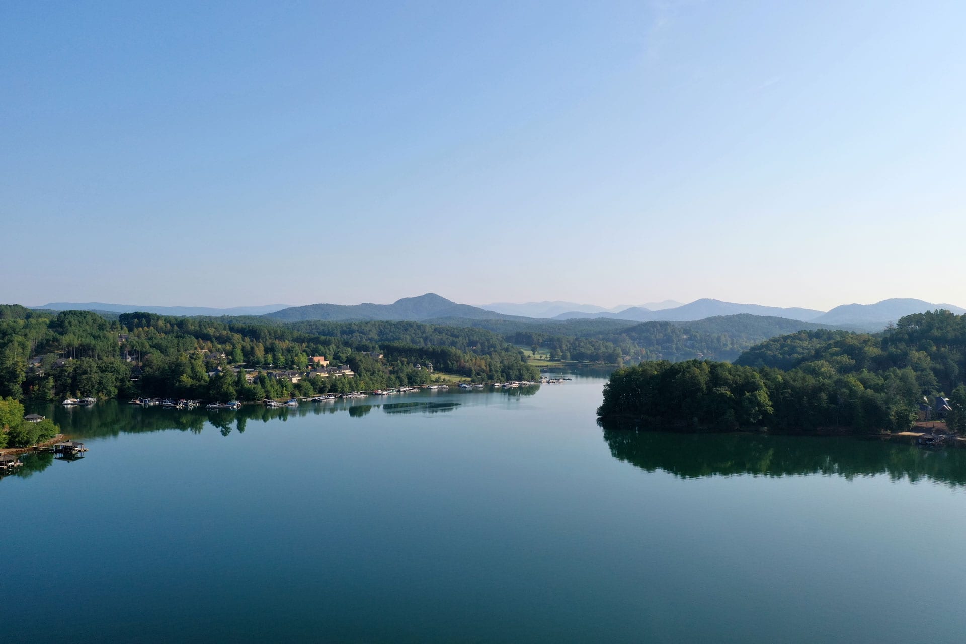Drone image of lake, trees and mountains in the distance.